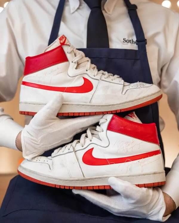 White and red Nike sneakers held by gloved auctioneer, symbolizing high sneaker value and rarity.